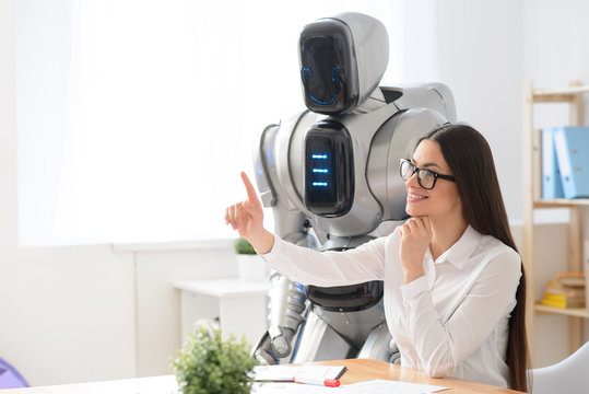 Pleasant girl sitting in the office with robot