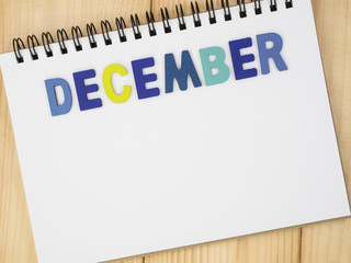 Word spelling month in the year December by wooden letters on notebook with wood background (Month name word series)