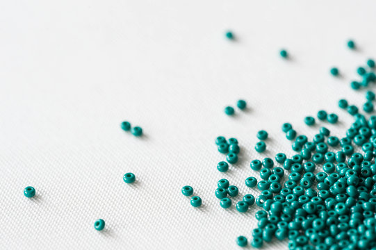 Scattered seed beads of emerald color on the textile background 