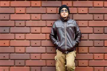 Obraz premium An Asian Man in a Brown Jacket Leans Against the Wall
