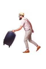 Young creative tourist man is posing with suitcase on grey background.