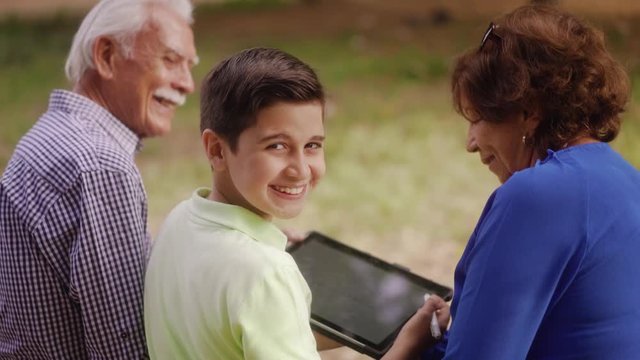 Happy boy smiling at camera, child portrait with grandfather and grandmother, kid studying for school homework with tablet pc. Old man, senior woman, family and generations, education