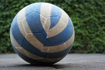 The blue and white soccer ball on the cobblestone road was forgotten by children. Green fence (hedge) is as background, Kuta, Bali, Indonesia. 
