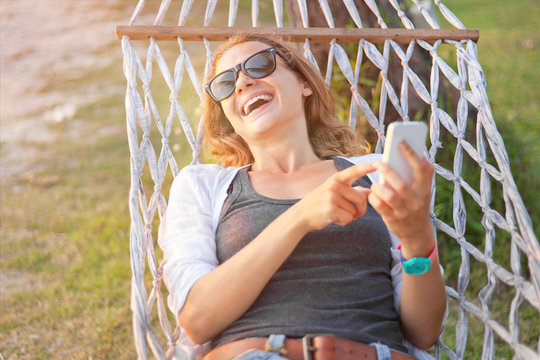Happy beautiful young woman with a mobile phone in a hammock. Su
