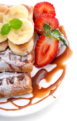 Sweet dessert:waffles with banana slices and strawberries and chocolate topping on a white background.