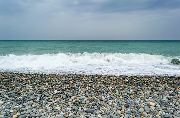 Waves breaking on lonely pebbles beach, forming sprays