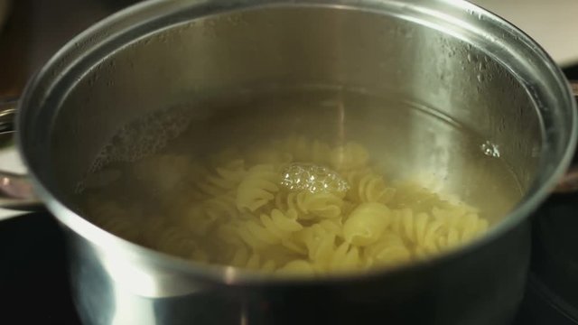 Boiling spiral pasta in the water in a metal pot 