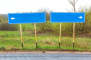 Blank direction blue signpost on the asphalt road on the background of green fields and bushes