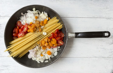 Cooking spaghetti with vegetables and herbs in the pan on white background