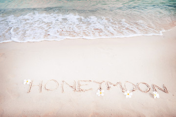 Inscription Honeymoon written on the sandy beach with ocean wave - free space. vintage color tone effect