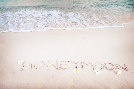 Inscription Honeymoon written on the sandy beach with ocean wave - free space. vintage color tone effect