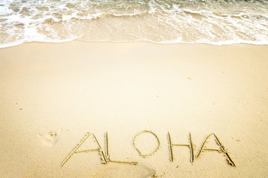 Inscription Aloha written on the sandy beach with ocean wave - free space. vintage color tone effect
