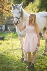 Young blonde woman posing outdoor with white horse. Farmer woman taking care of her horse.