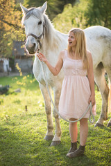 Young blonde woman posing outdoor with white horse. 