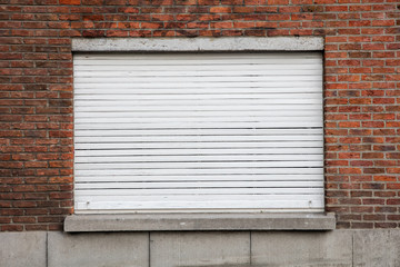 Geschlossener Fenster mit weißem Rollladen auf roter Backsteinfassade
