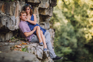 Obraz na płótnie Canvas Young beautiful tender modern stylish couple of slim woman and man sitting on rock with near big stony grey wall on outdoor