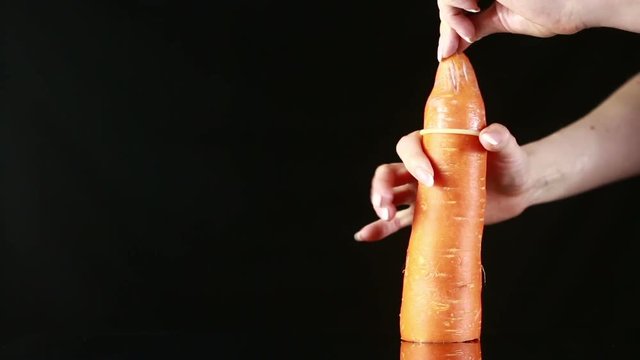 Orange carrot with a condom on a black background