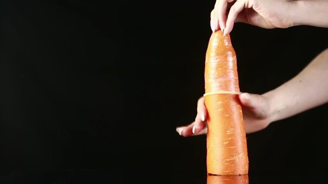 Orange carrot with a condom on a black background