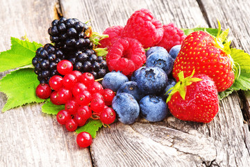 frische Sommerfrüchte: Erdbeeren, Himbeeren, Heidelbeeren, Johannisbeeren, Brombeeren, frisch gepflückt, mit Blättern, Copyspace, auf Holz