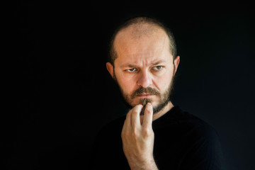 Naklejka premium Serious man with beard and mustaches on black background in low key, holding arm on chin, thoughtful