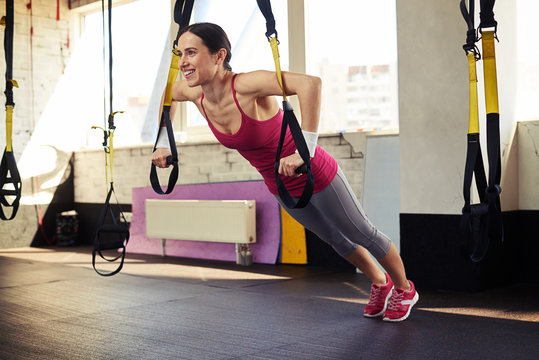 Young brunette is pushing at the trx