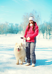 Woman owner and white Samoyed dog on leash walking in winter par