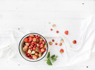 Wild strawberries in rustic metal bowl on white wooden background