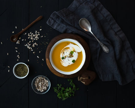 Pumpkin soup with cream, seeds and spices in rustic metal bowl over black background. Top view.