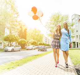 Two young blond women holding colorful latex balloons.