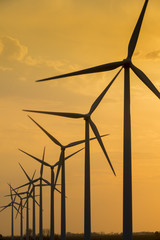 Obraz premium Windmill wind turbine generating power turning silhouetted against sunset sky