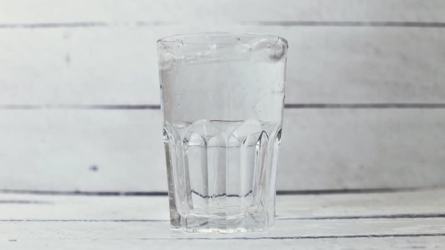 Water is poured into a transparent glass on a white background wood