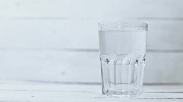 Water is poured into a transparent glass on a white background wood