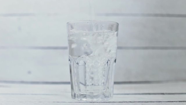 Water is poured into a transparent glass on a white background wood