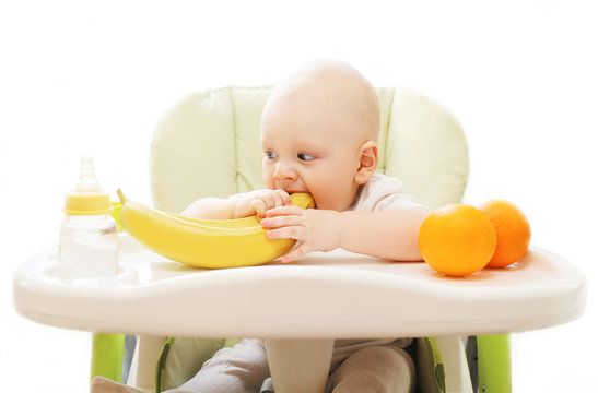 Baby bites banana fruits at the table home