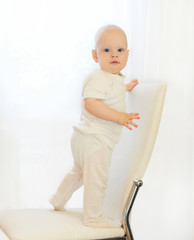 Baby stands on the chair at home and looks on camera