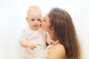 Happy mother hugging kissing her baby over window