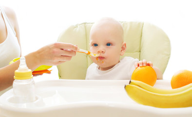 Mother feeds baby spoon on the table at home