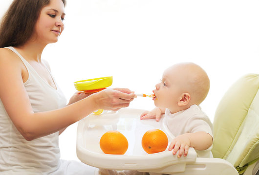 Mother feeds baby spoon on table at home