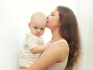 Young mother hugging kissing her baby over window