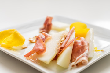 Prosciutto slices with yellow lemon on white plate wih seeds and peel. Very soft focus.