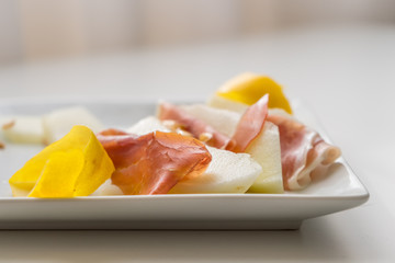 Detail of prosciutto slices with water melon. Peel and seeds. Starter in very soft focus on white plate.