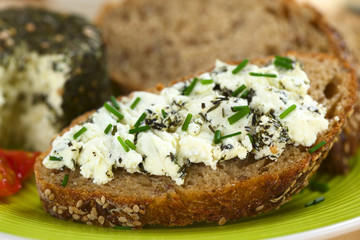 Slice of wholegrain bread spread with goat cheese with herbs with chives on top (Selective Focus, Focus on the front of the cheese)