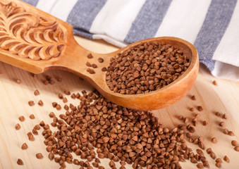 uncooked buckwheat grains in wooden spoon on wooden table
