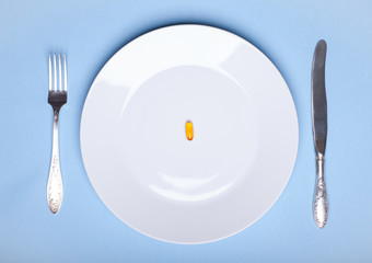 One pill on white dinner dish with flatware on blue background