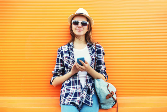 Pretty smiling woman using smartphone in city over orange backgr