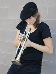 Female trumpet player blowing her horn outside.