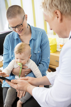 Doctor Showing Tablet Computer To Woman With Baby