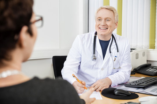 Male Doctor Looking At Female Patient At Desk