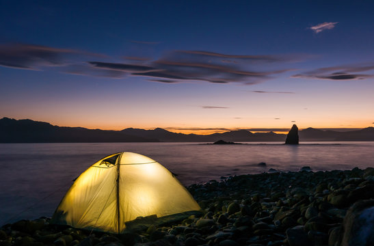 A camping tent glows under a night sky on the Pacific coast of Kamchatka. Outdoor Camping adventure. Kamchatka peninsula, Russia (nights shot, long exposure)