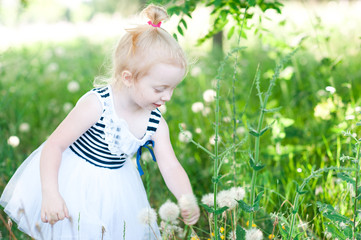 Funny baby girl 2-3 year old playing outdoors. Wearing stylish striped dress. Walking in meadow. Childhood.